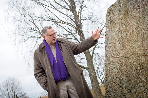 A researcher points at a runic stone in a forest